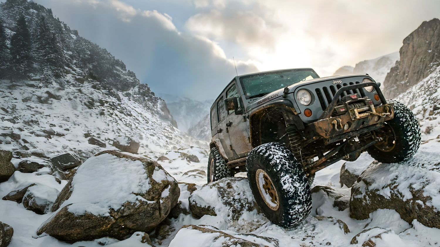 Jeep driving on a snowy mountain road with rocky terrain